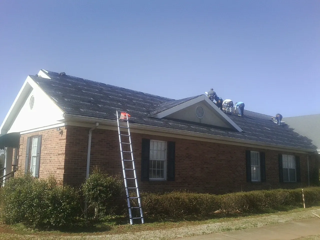 Crew tearing shingles off a brick ranch roof with a ladder set — Metal Roof Repair work by our crew in Lyle