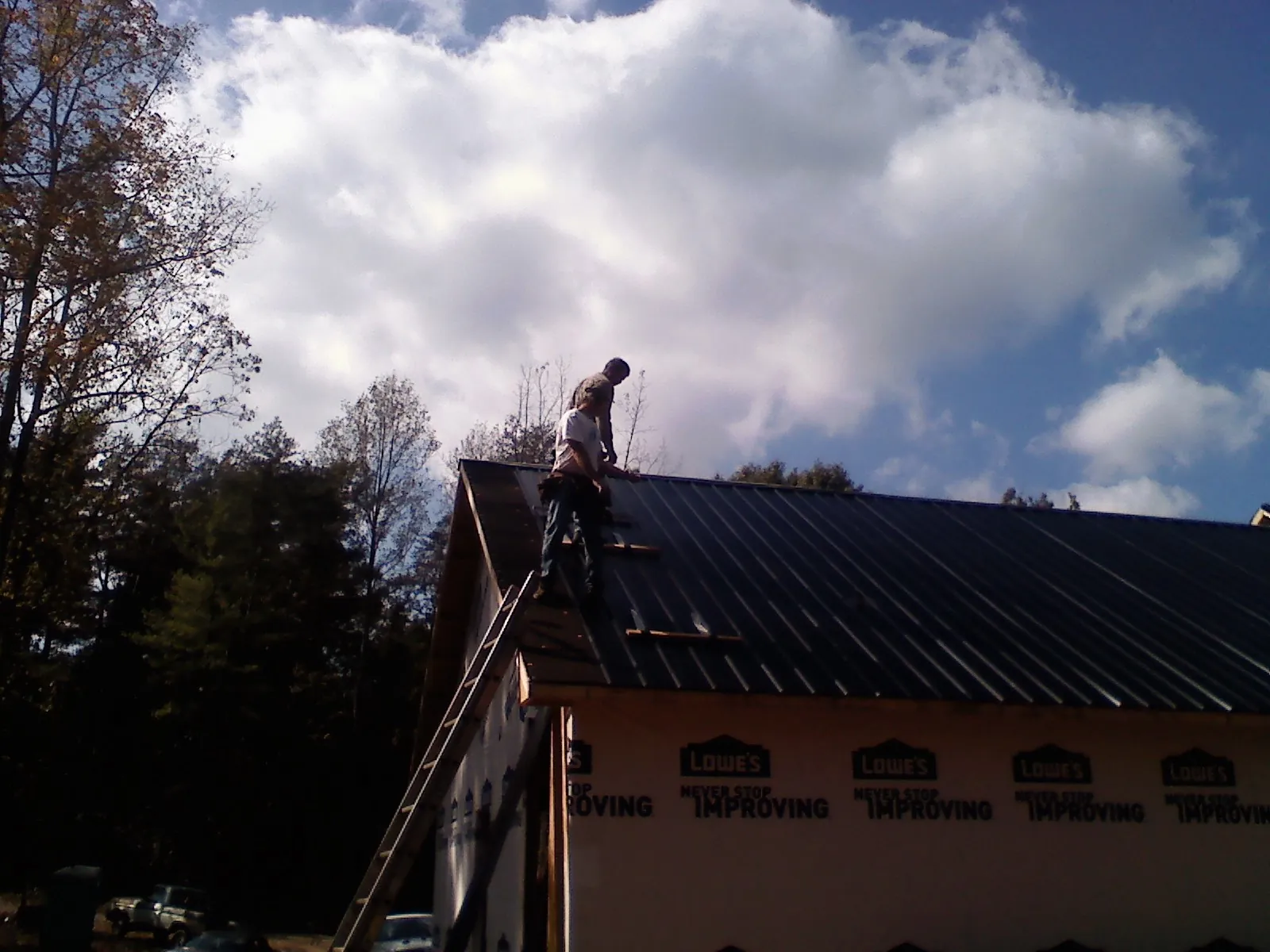 Roofer fastening dark metal panels high against a cloudy sky, from a Roof Inspection job in Lyle